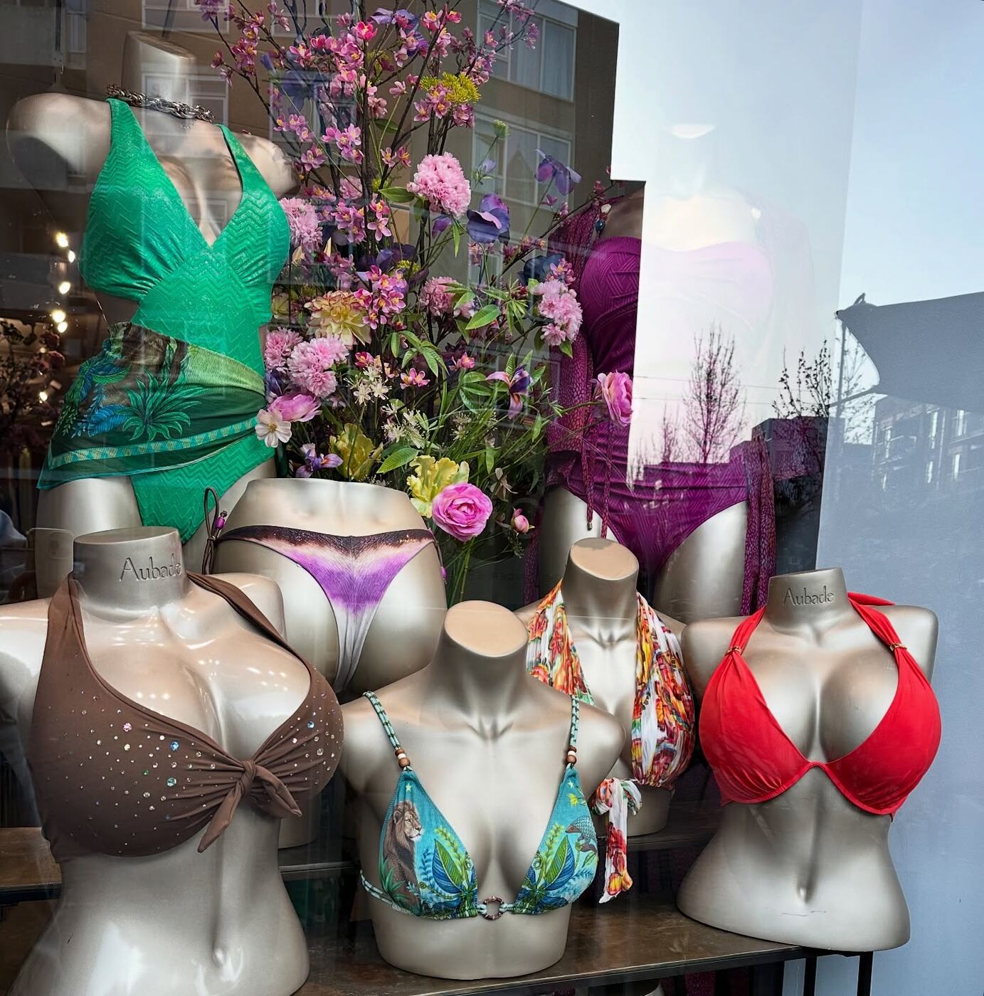 Manichini con costumi da bagno colorati tra i fiori nella vetrina della boutique