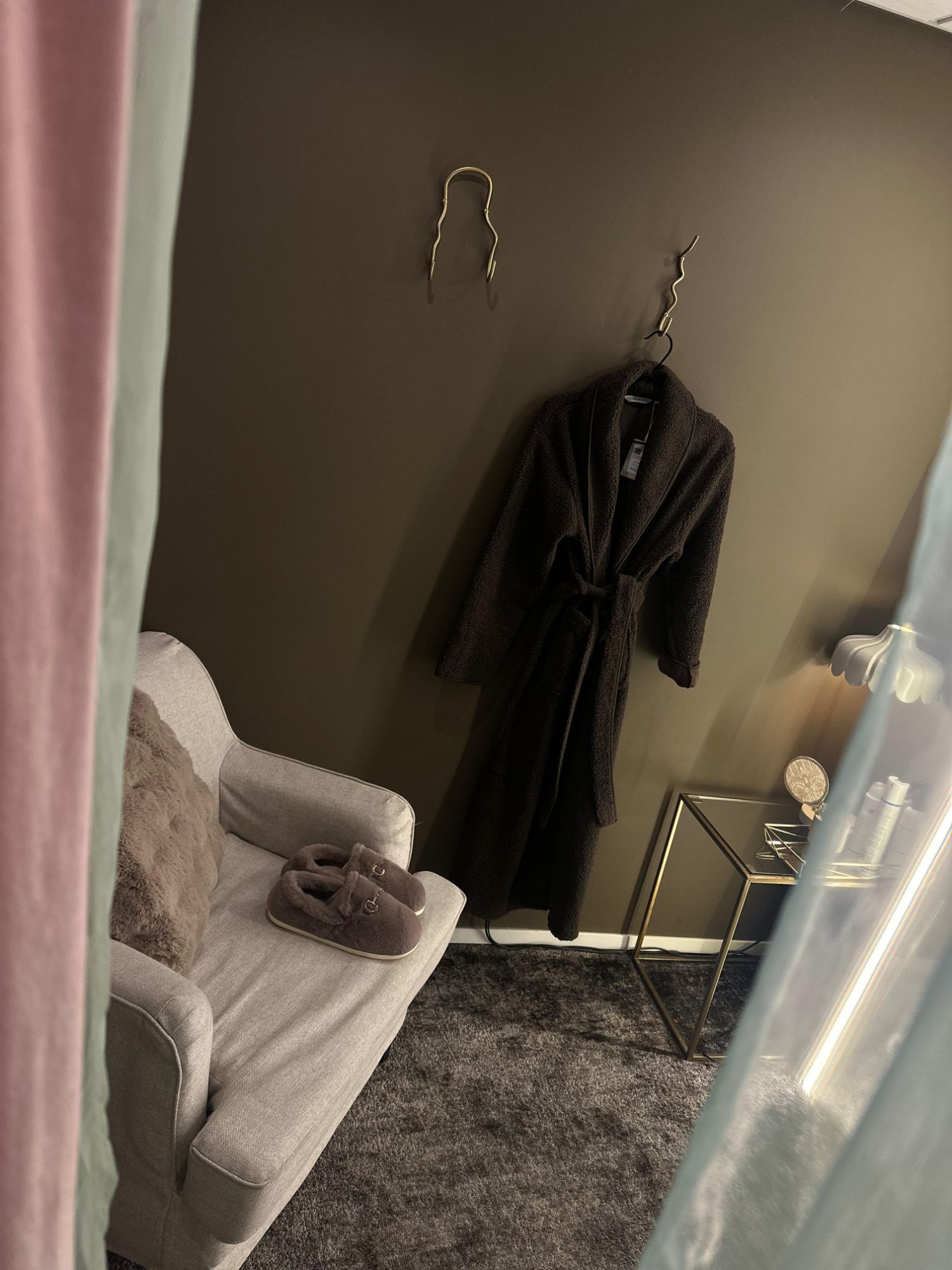 A cosy fitting room with a soft bathrobe, slippers and an armchair